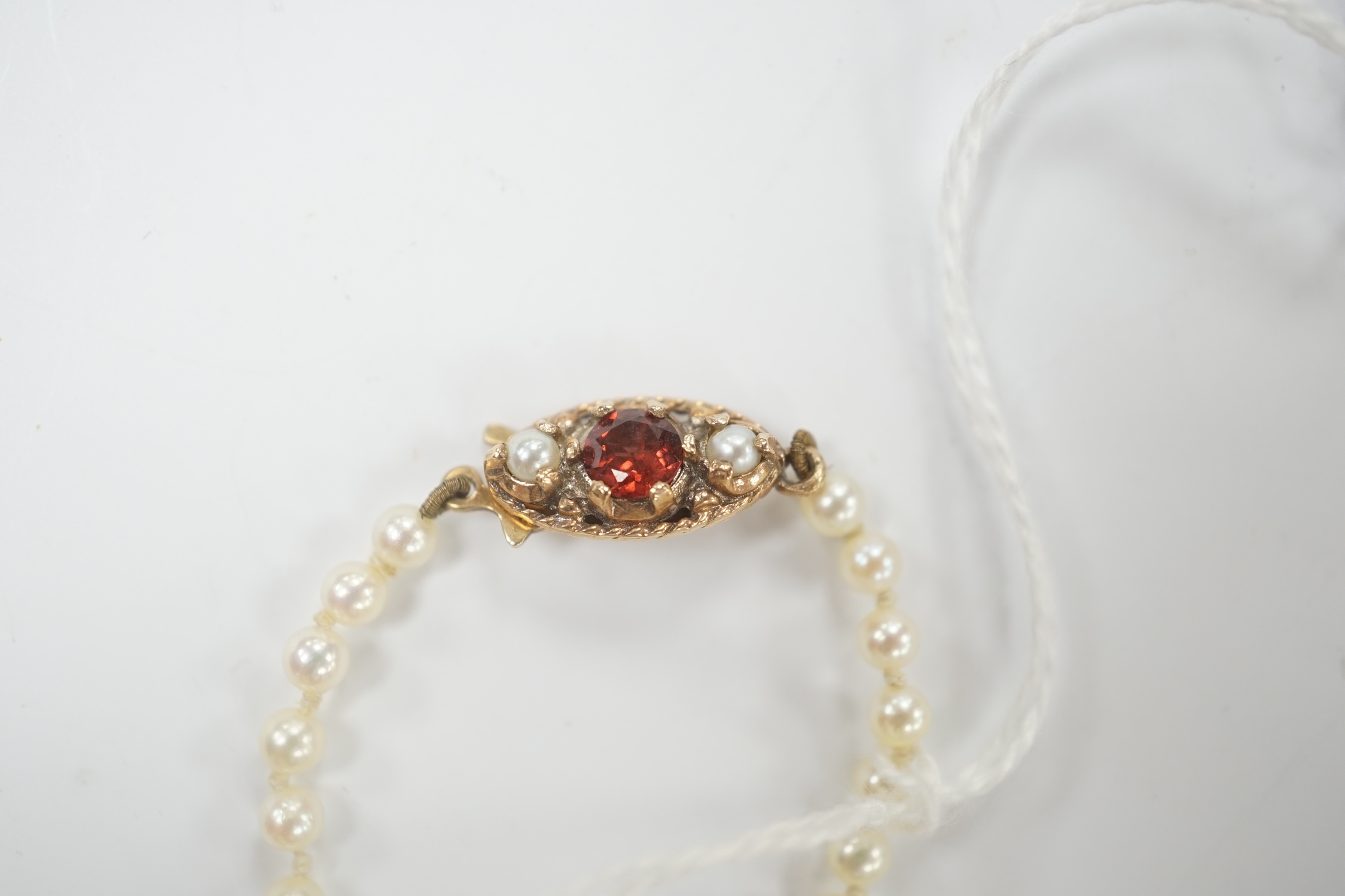 A single strand graduated cultured pearl necklace, with garnet and seed pearl set 9ct gold clasp, 52cm.